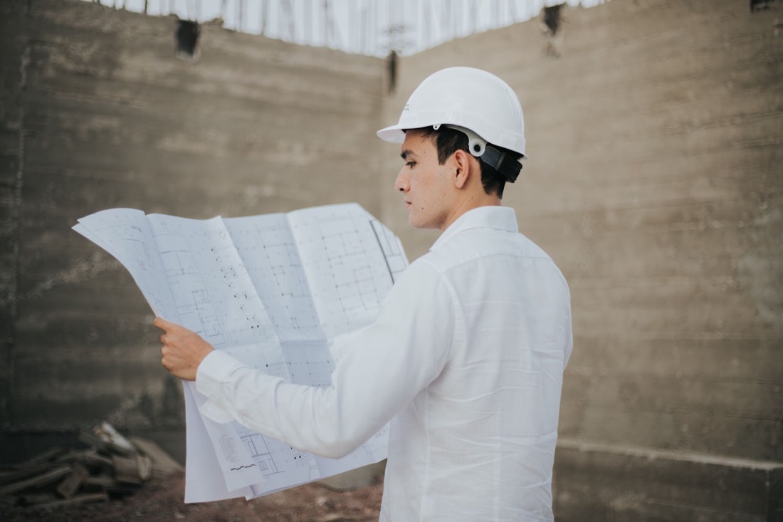 A contractor in a hard hat reads a large set of building plans on site.
